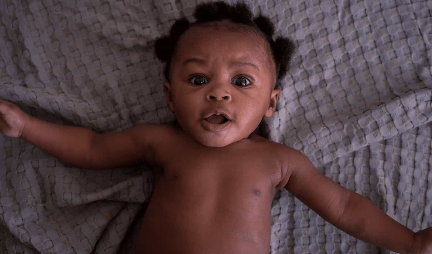 A laughing baby sitting on floor with legs wide spread while his hands touching the Huggies diapers